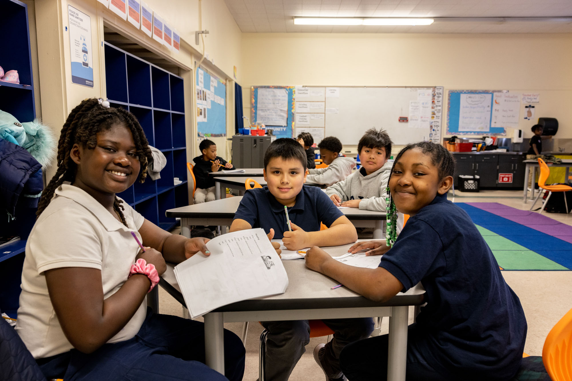 Three youth sitting a desk in a classroom posing for a photo