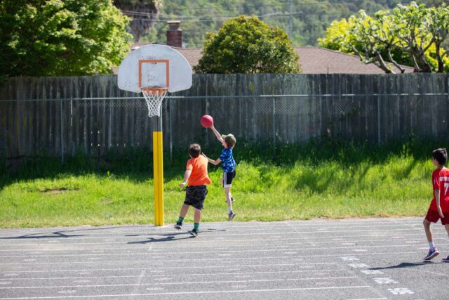 Children playing basketball outside together.