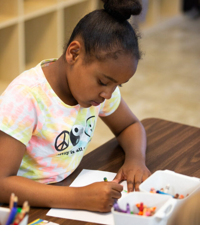 A child drawing with crayons at an after school program.