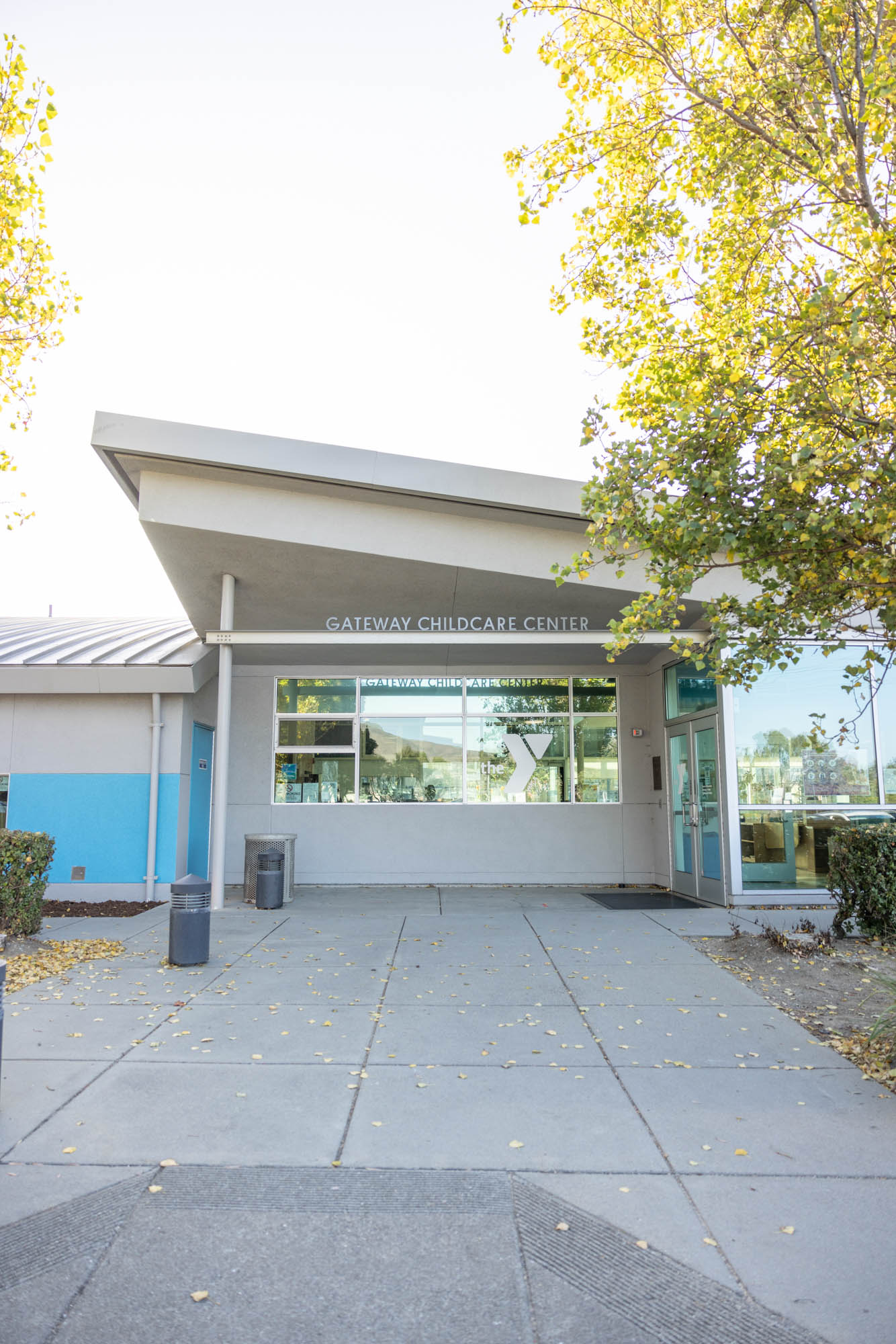 Exterior view of the Gateway Childcare Center, showing a modern building with large windows, an angular roof, and a surrounding sidewalk with trees and shrubs.