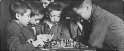 A group of young boys gather closely around a chessboard, deeply focused on the game being played.