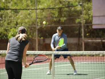 Adult male and female playing tennis on a tennis court.