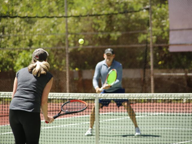Adult male and female playing tennis on a tennis court.
