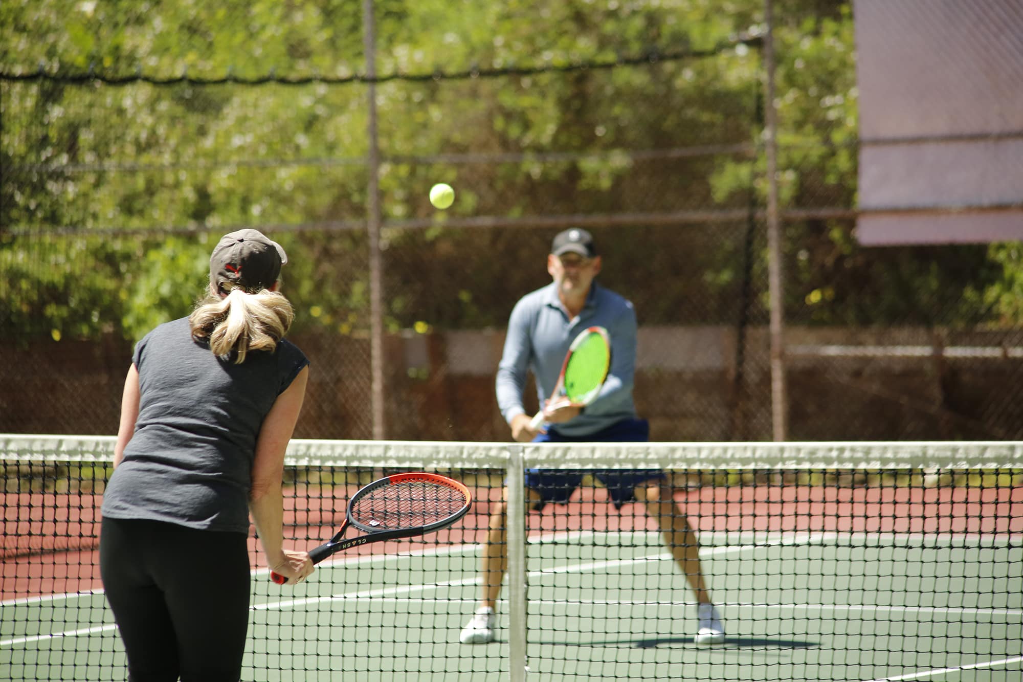 Adult male and female playing tennis on a tennis court.