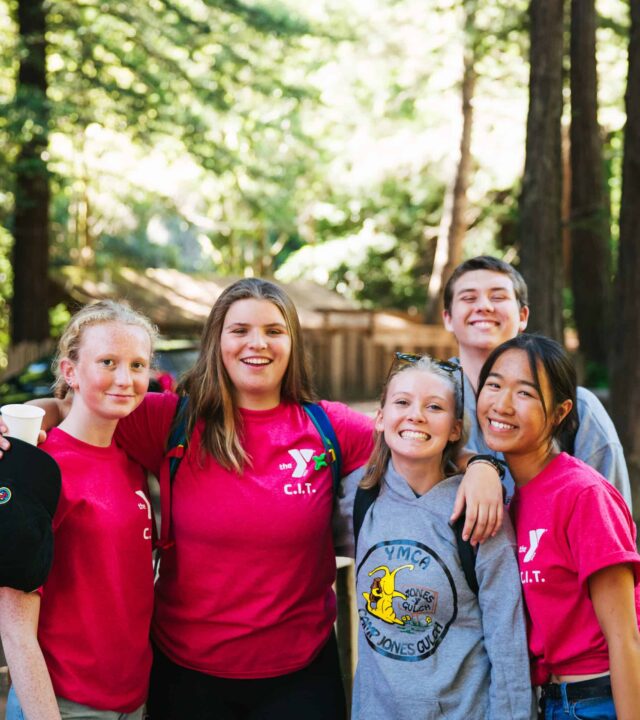 A group of teenage girls and boy posing for photograph in the woods