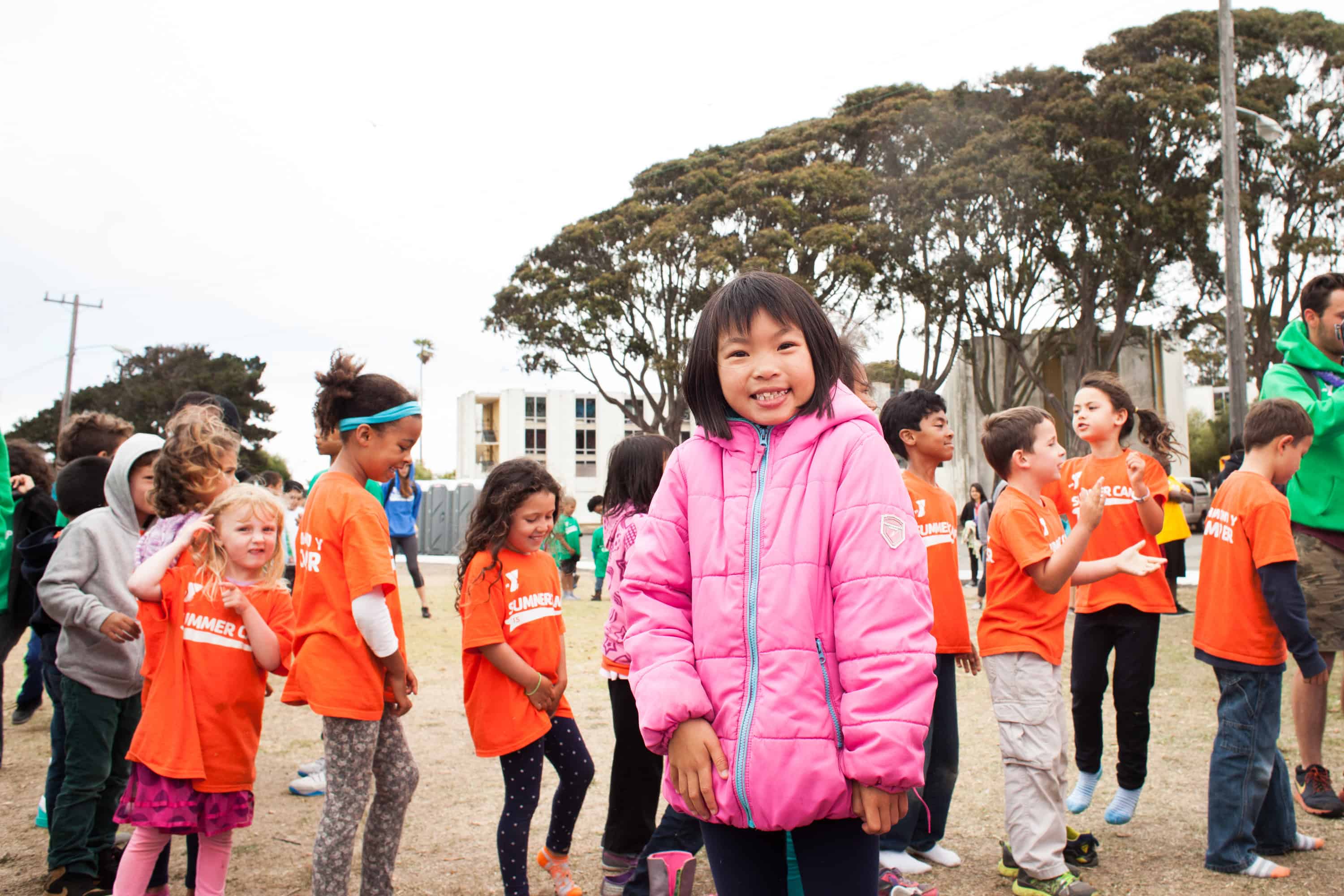 Young girl outdoors at a summer camp event wearing a pink jacket.