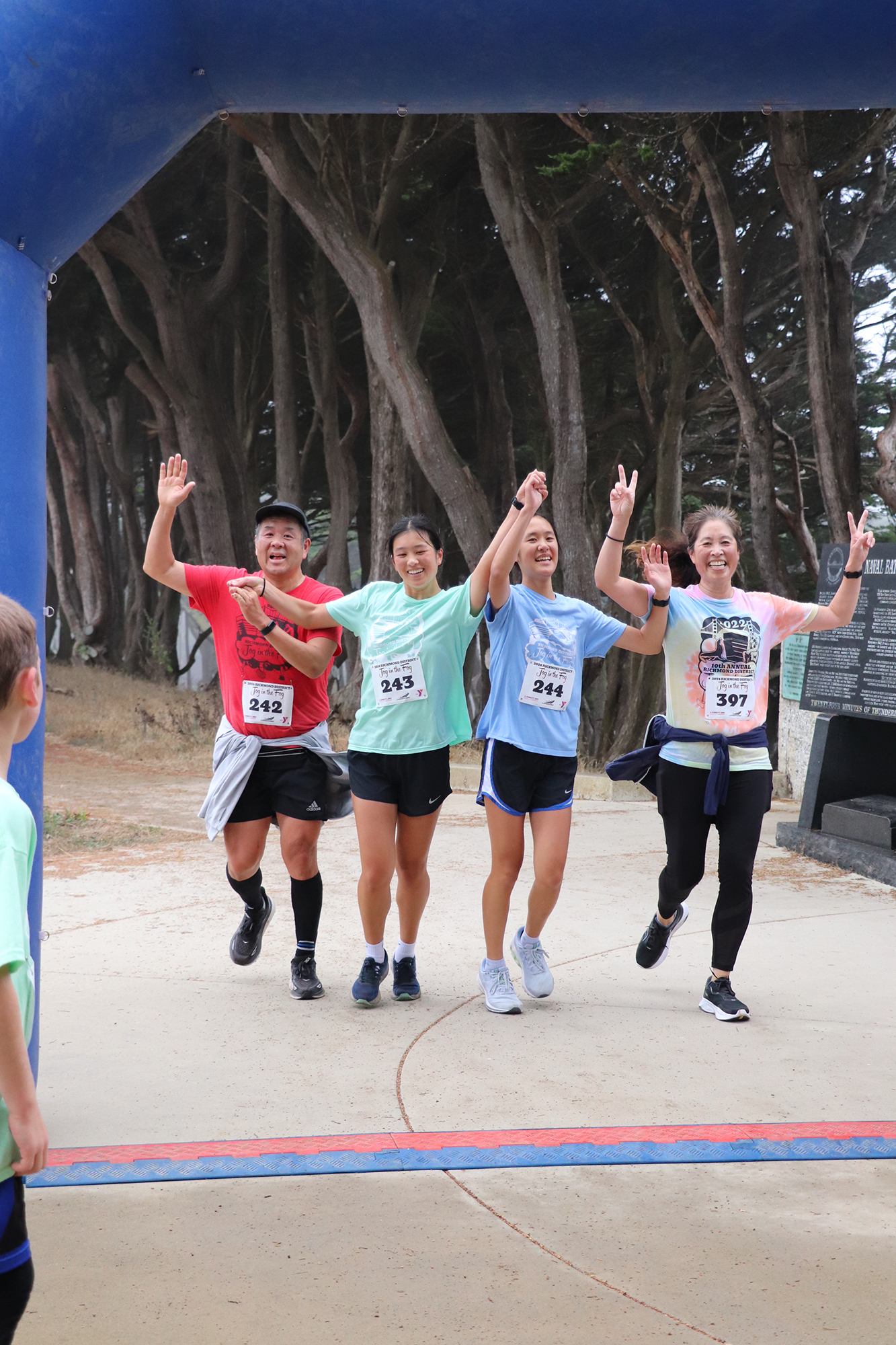 A male and three females with their arms raised as they run across a finish line.