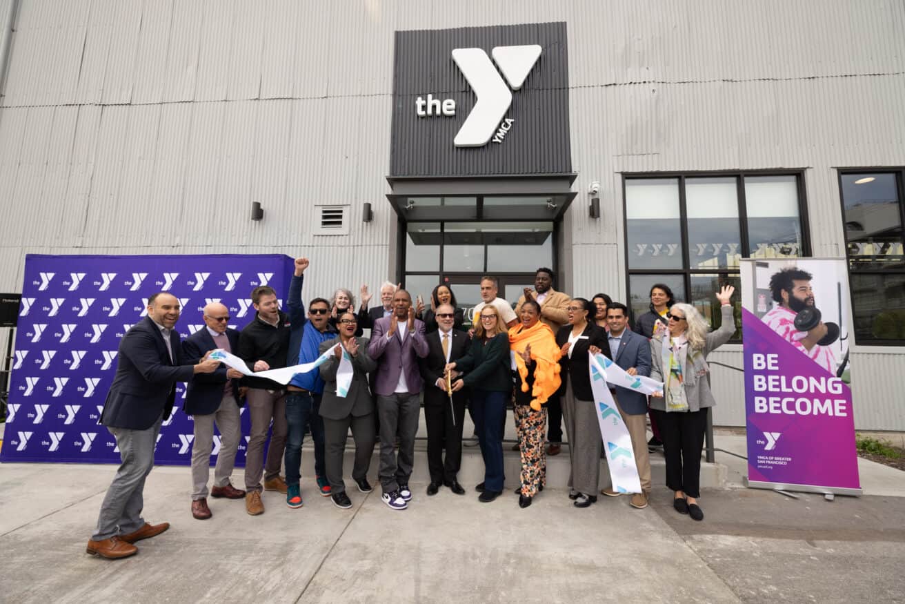 A group of people gathered around to cut a ribbon to celebrate the grand opening of the Dogpatch YMCA.