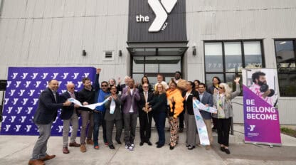 A group of people gathered around to cut a ribbon to celebrate the grand opening of the Dogpatch YMCA.