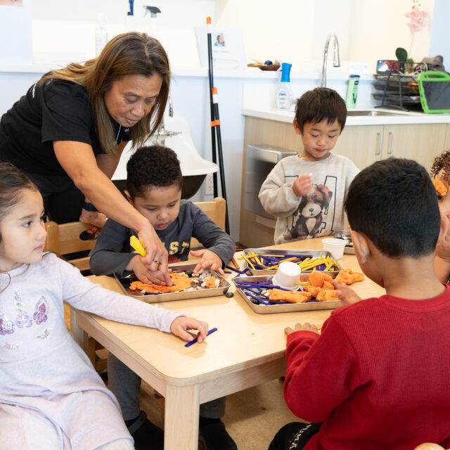 An adult female helping youth with a play dough project.