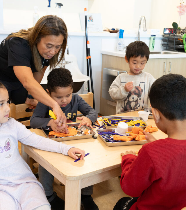 An adult female helping youth with a play dough project.