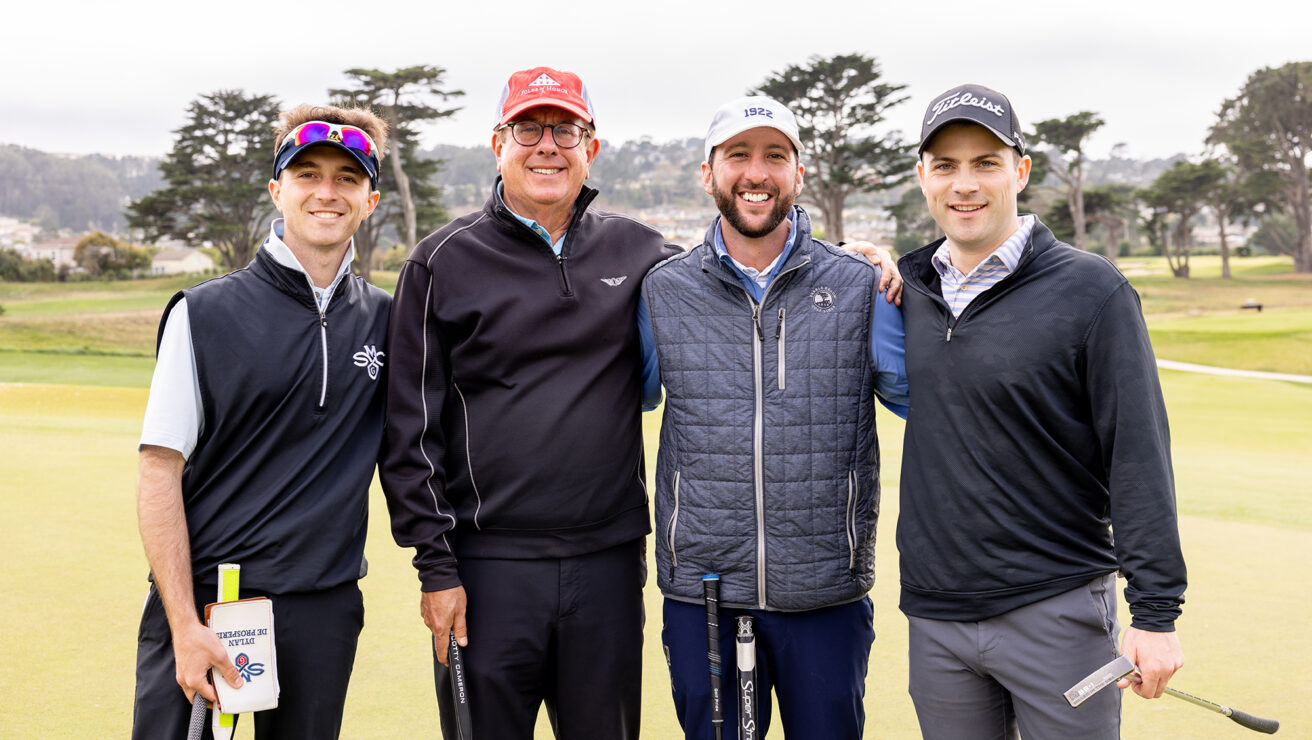 Four adult males posing for a photo at a golf course.