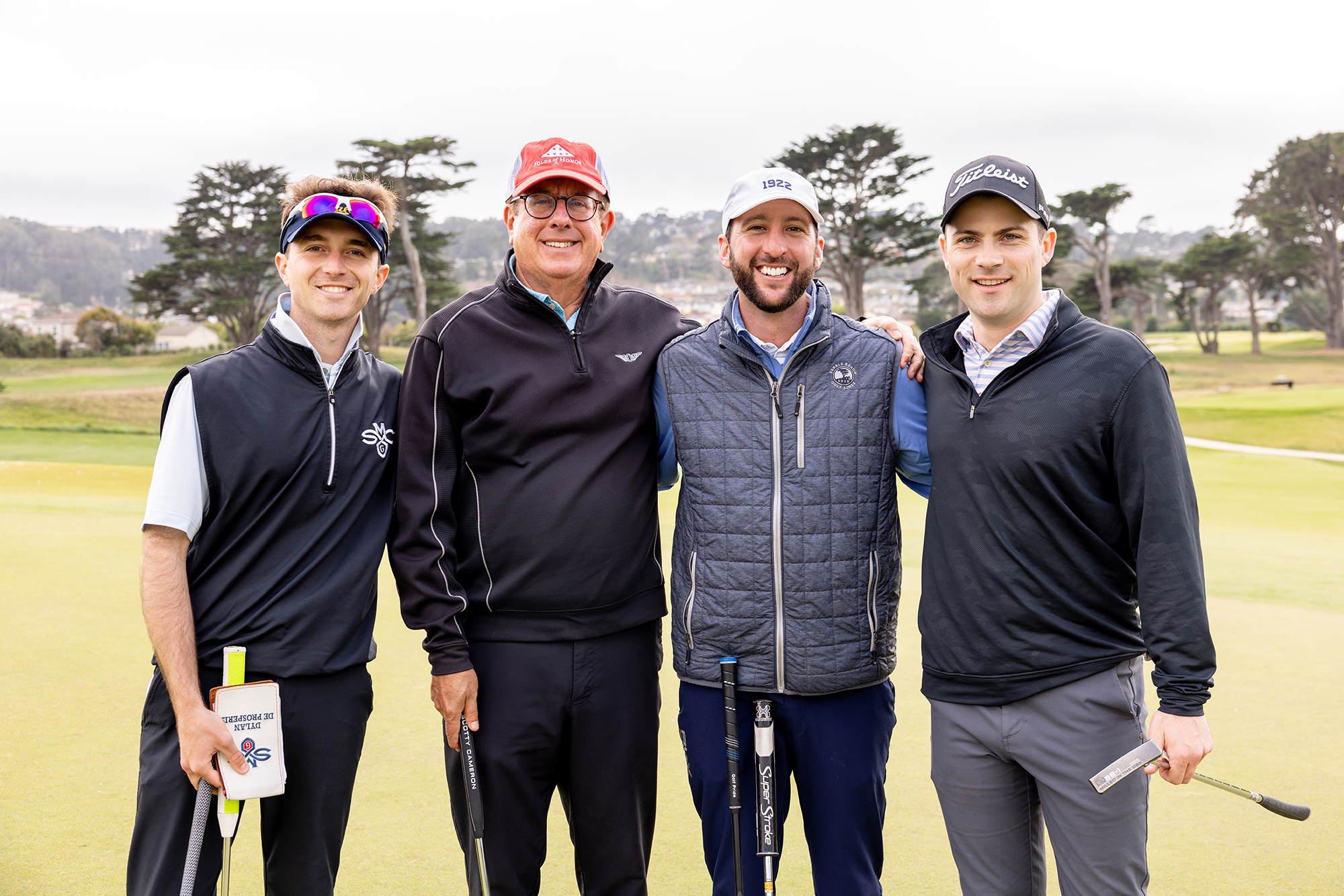 Four adult males posing for a photo at a golf course.