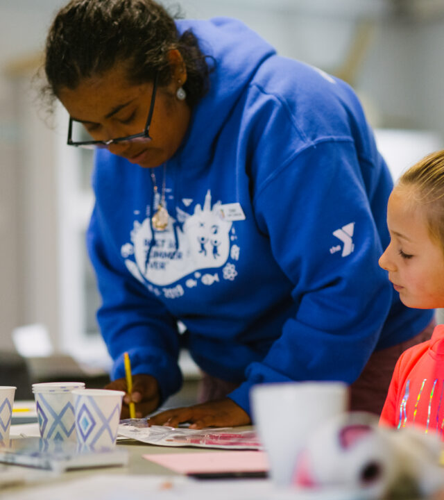 Presidio Community YMCA - A woman YMCA staff member is writing while a youth program participant is watching.