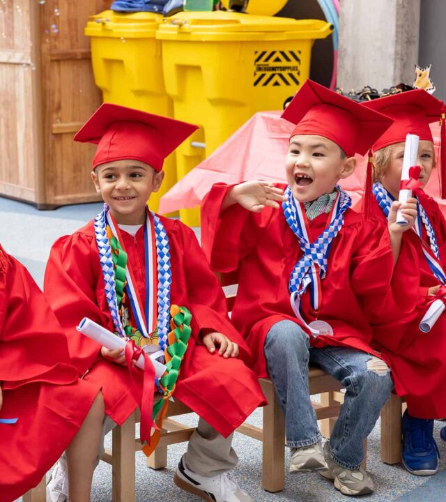 A group of youth wearing red caps and gowns at a graduation ceremony.