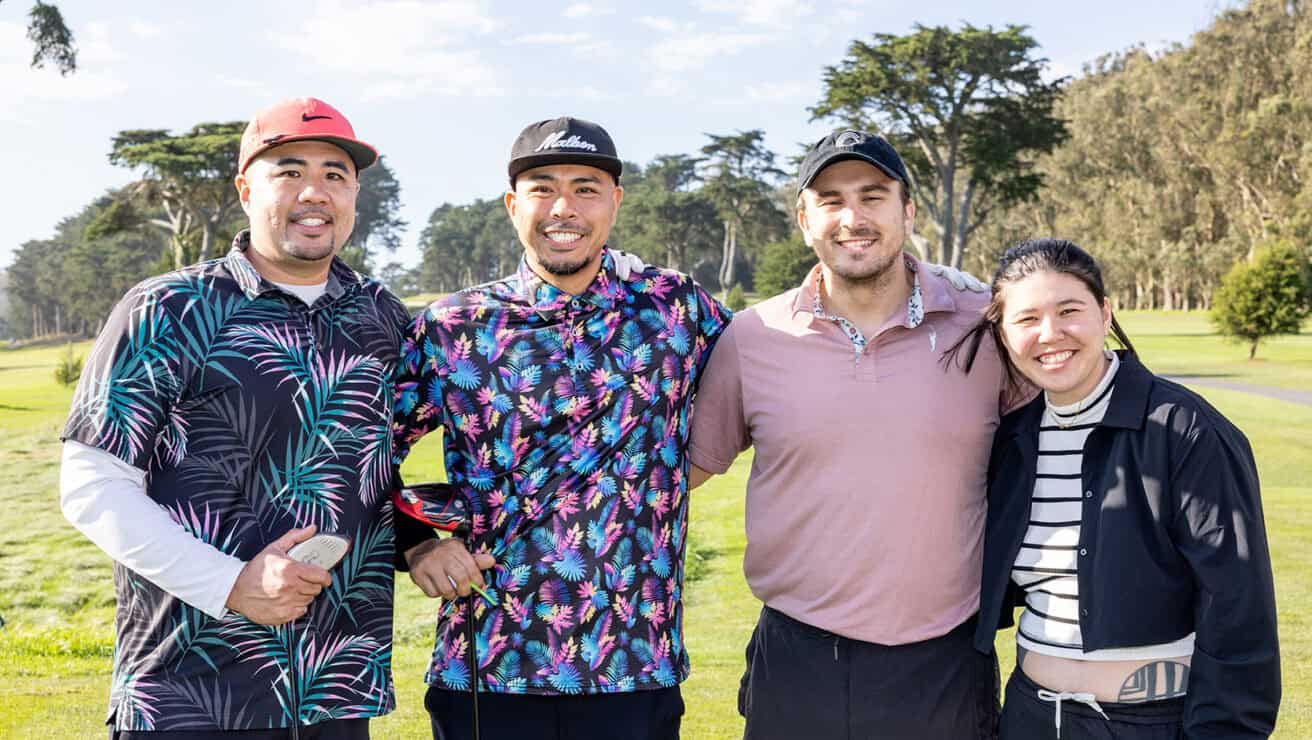 A group of three adult males and one adult female posing for a photo on a golf course.
