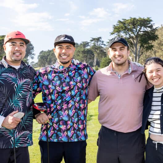 A group of three adult males and one adult female posing for a photo on a golf course.