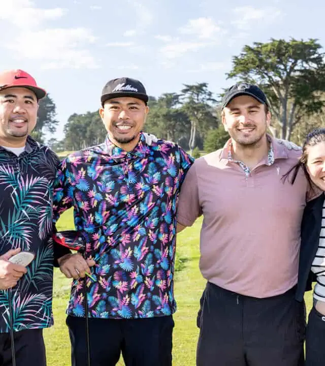 A group of three adult males and one adult female posing for a photo on a golf course.