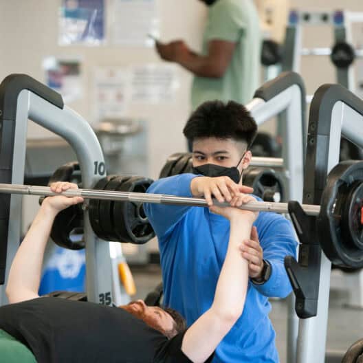One adult male showing another adult male a weight lifting technique.