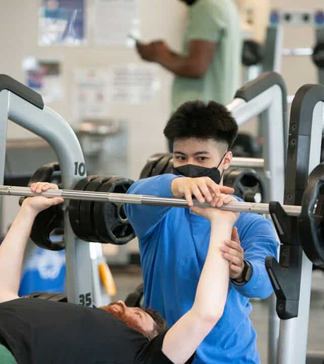 One adult male showing another adult male a weight lifting technique.