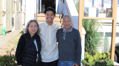 Three people are standing outdoors in front of stairs, smiling at the camera. The person in the middle wears a traditional barong tagalog, while the others wear casual clothes, enjoying a moment of wellness near the Marin YMCA.