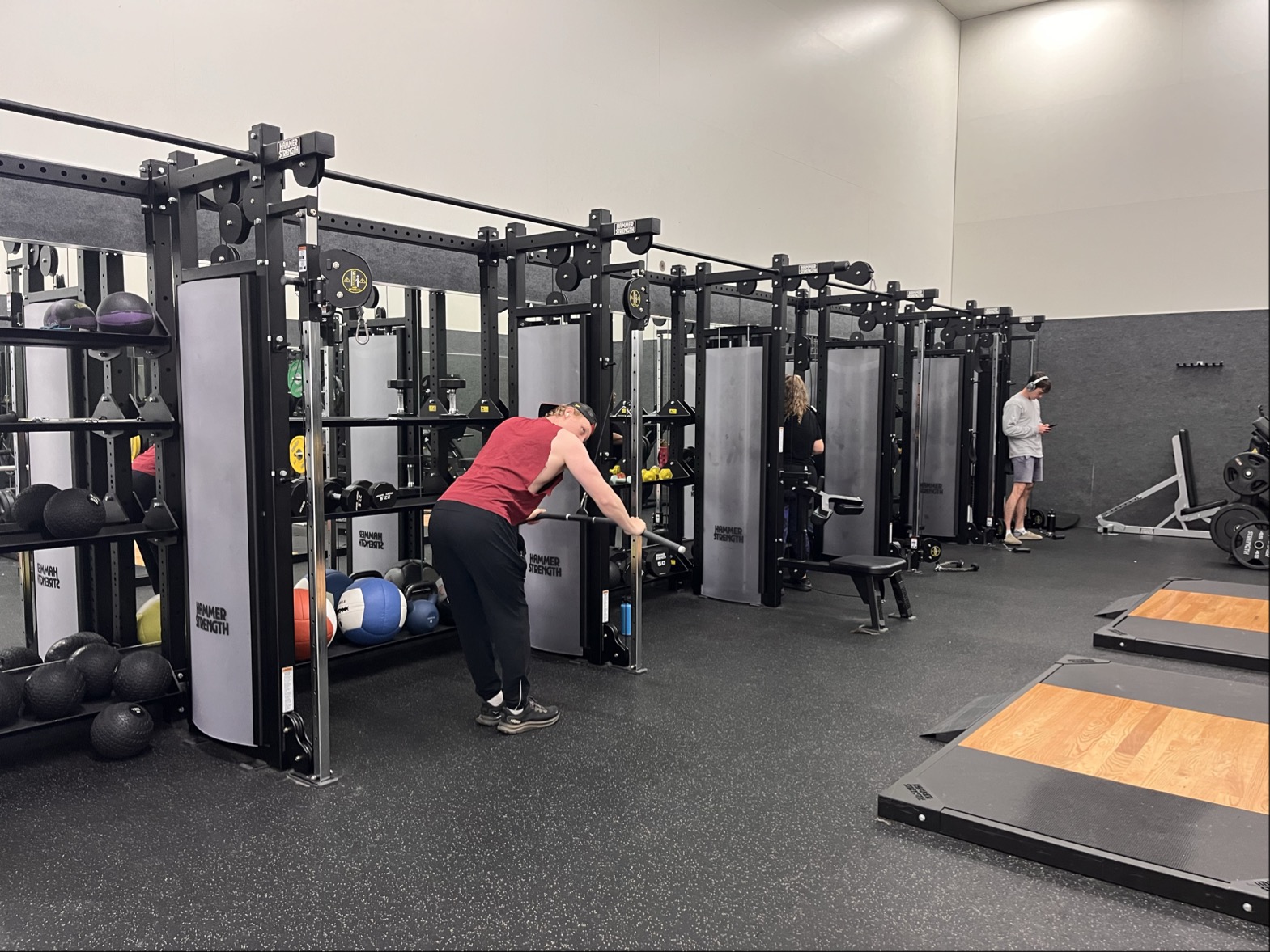 Three people exercise individually at the Marin YMCA gym, using medicine balls, resistance machines, and a treadmill in a spacious, well-lit room with updated facilities that support overall wellness.